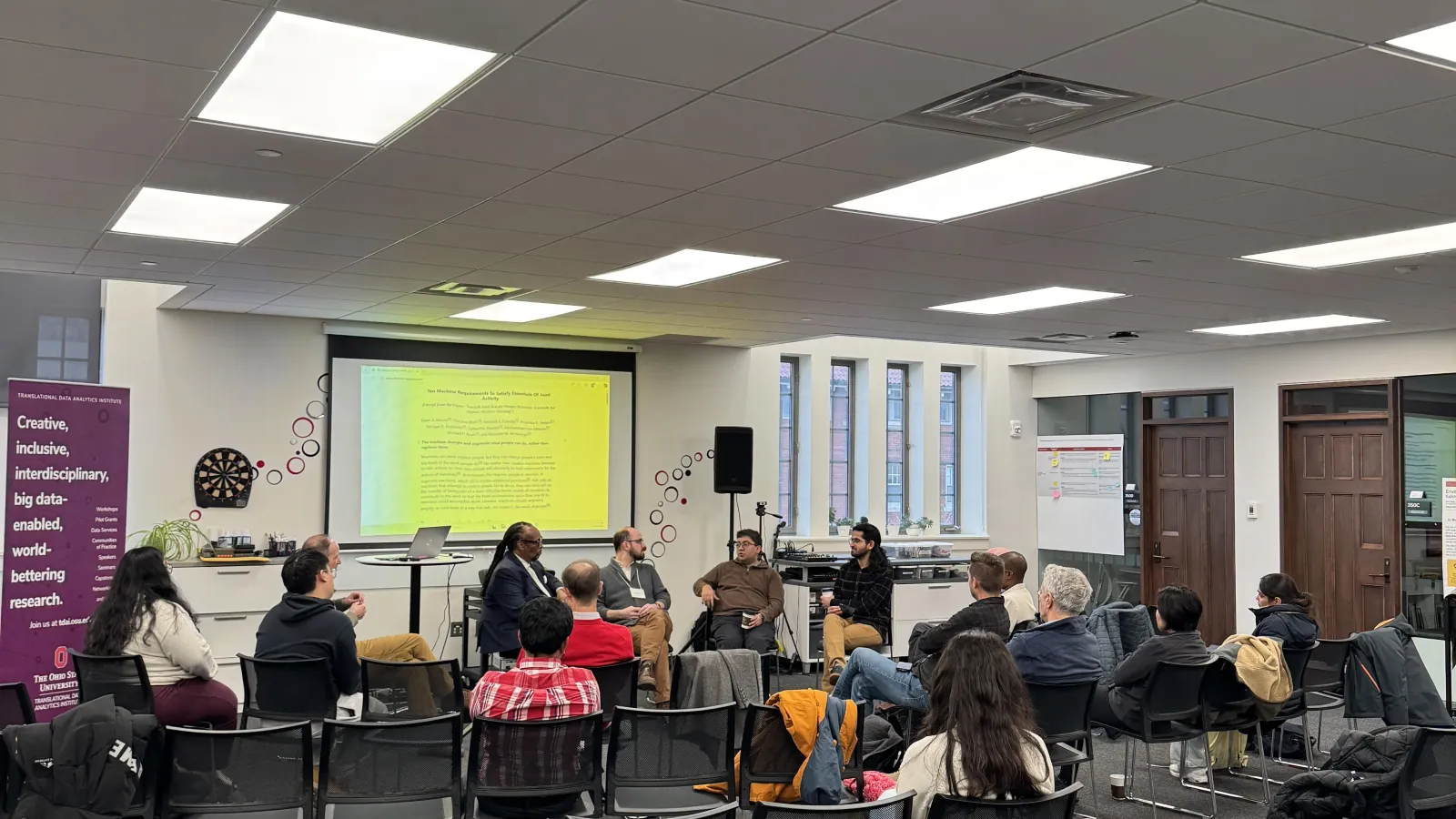 Audience members seated in a semi-circle listen to a panel discussion on human–AI systems in a collaborative event space at Ohio State.